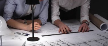 Mimarlar birlikte çalışır, bina planlarını ve planlarını analiz eder, bir ofiste tasarım kavramlarını ve mühendislik unsurlarını tartışırlar..