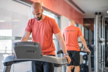 Spor salonunda koşu bandına hazırlanan bir adam.