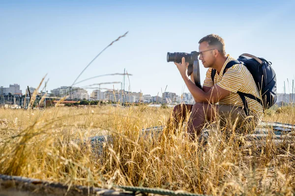 Fotograf Batohem Sedícím Suché Trávě Ukazujícím Před Sebe Kameru Městem — Stock fotografie