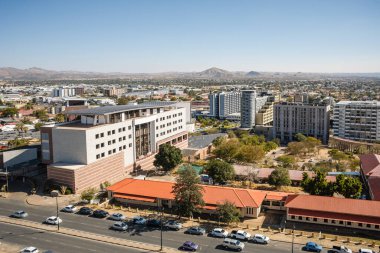 Modern şehir merkezi Windhoek, Namibya, yüksek çağdaş binalar, geniş sokaklar, hareket eden arabalar, ve açık mavi bir gökyüzü.