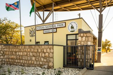 Okaukuejo Kamp Girişi, Etosha Milli Parkı, Namibya - 19 Ağustos 2025: Taş kapıya ve akşam ışığı olan kuleye giden asfalt yol.