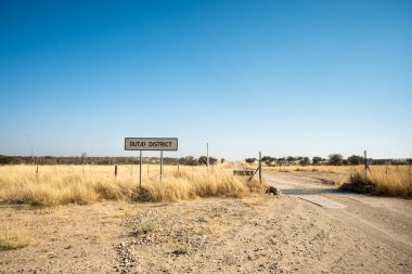 Namibya 'daki Outjo Bölgesi savanasına giden toprak yolda açık çayırlar ve dağınık ağaçlarla çevrili bir yol işareti var..