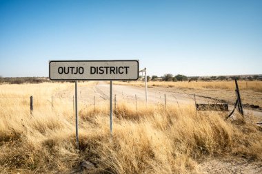 Namibya 'daki Outjo Bölgesi savanasına giden toprak yolda açık çayırlar ve dağınık ağaçlarla çevrili bir yol işareti var..