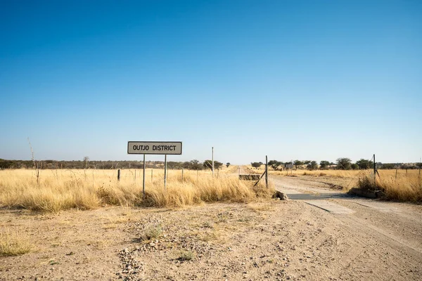 Namibya 'daki Outjo Bölgesi savanasına giden toprak yolda açık çayırlar ve dağınık ağaçlarla çevrili bir yol işareti var..