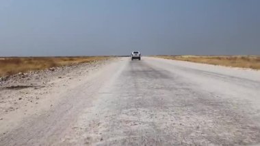 20 Ağustos 2025 'te, açık mavi gökyüzünün altında, Namibya' daki tozlu bir çakıl yolunda ilerleyen beyaz bir kamyonet. Uzak yolculukların, maceraların ve kırsal alanların özünü yakalar.