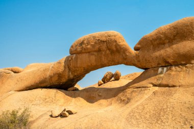 Namibya 'daki Spitzkoppe Halk Kampı' nda Granit tepeler ve engebeli çöl manzaraları. Dağılmış akasya ağaçlarıyla altın çayırlar, berrak gökyüzünün altındaki dramatik kayalık dağlara karşı tezat oluşturuyor..