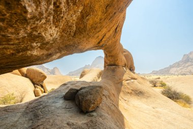 Namibya 'daki Spitzkoppe Halk Kampı' nda Granit tepeler ve engebeli çöl manzaraları. Dağılmış akasya ağaçlarıyla altın çayırlar, berrak gökyüzünün altındaki dramatik kayalık dağlara karşı tezat oluşturuyor..