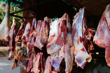 Geleneksel pazar ortamında metal kancalardan sarkan büyük et parçaları. Et taze görünüyor, görünür yağ ve kas dokusuyla..