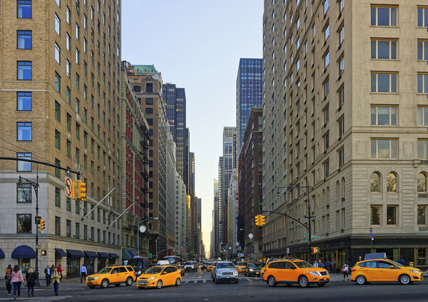 New York, USA - May 7, 2015: Crossroad on 6th avenue in Midtown Manhattan, New York, USA. Road leading to Central Park South. Heavy traffic on the road, especially taxi cars. And many tourists passing by.