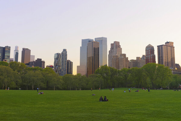 Tourists relaxing on the green lawn and Midtown Manhattan skyline in Central Park South, in New York, USA.