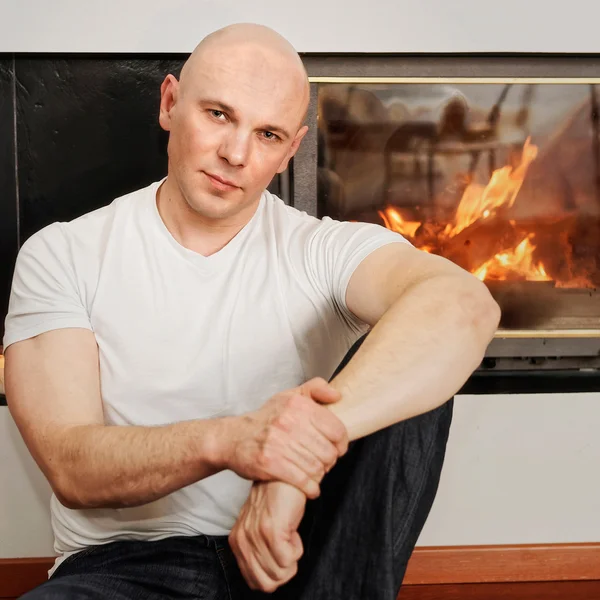 Handsome bald headed man sitting on fur carpet at fireplace — Stock Photo, Image