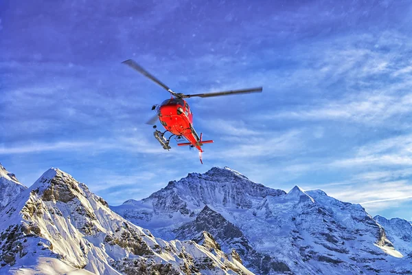 Czerwony helikopter na niebie w szwajcarskich Alpach w pobliżu zimą — Zdjęcie stockowe