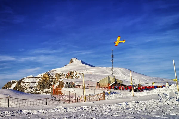 Avion jaune survolant la station alpine dans les Alpes suisses en hiver — Photo