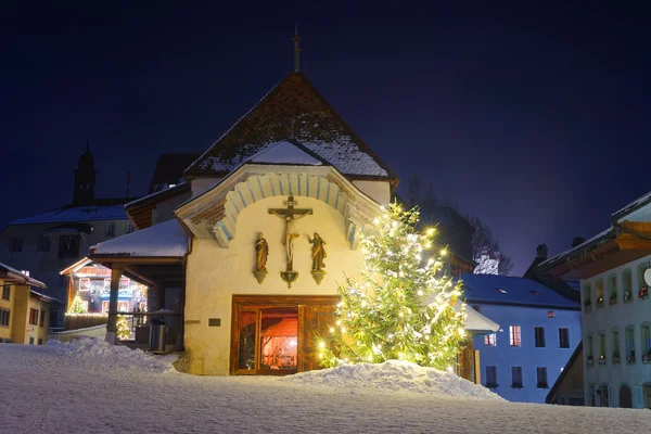 Illuminated Christmas fir tree in front of the church in Gruyere