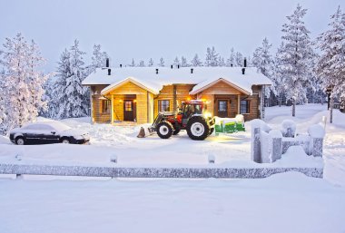 Tractor is clearing away snow at the Wooden Cottage in Ruka in Finland clipart