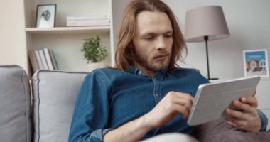 Kot gömlekli, uzun saçlı yakışıklı beyaz adam sosyal ağlarda tablet kullanarak haberlere bakıyor..