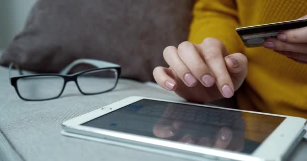 Großaufnahme einer Frau im gelben Pullover mit neutraler Maniküre, die Daten auf dem Tablet eingibt und die Bankkarte in der Hand hält. Online-Einkauf von zu Hause aus. — Stockvideo