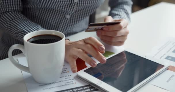 Close-up van vrouwelijke handen op bureaubladachtergrond met kopje koffie met bankkaart in handen en invoeren van gegevens op tablet. — Stockvideo