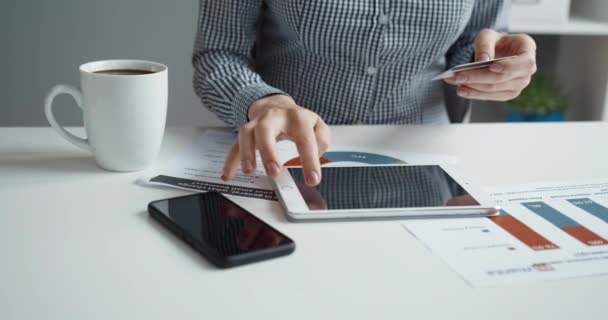 Close-up van vrouwelijke handen op bureaubladachtergrond met kopje koffie en smartphone met bankkaart in handen en invoeren van gegevens op tablet. — Stockvideo