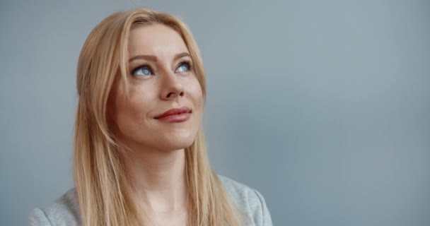 Retrato de una joven mujer caucásica con el pelo rubio mirando por la ventana sonriendo gira la cabeza y mira a la cámara. — Vídeos de Stock