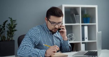 İş yerinde gözlüklü, genç ve zeki bir yönetici müşterisiyle cep telefonuyla konuşuyor. Uzaktan danışma.