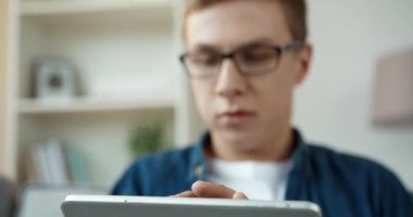 Kot gömlekli genç adam sosyal ağlarda arkadaşlarıyla sohbet ediyor. Evde kanepede otururken tablet kullanıyor..