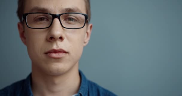 Close up retrato de jovem bonito cara em camisa jeans e óculos olhando para a câmera e sorrindo. — Vídeo de Stock