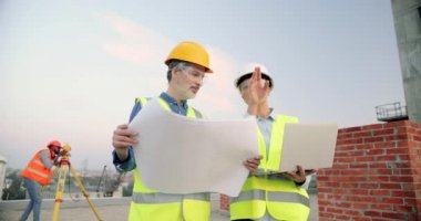 Beyaz erkek ve kadın müteahhitler, inşaat alanındaki taslak planına ve tablet cihazına sahip mimarlar. İnşaatta çalışan kadın ve erkek inşaatçılar. Dağılım.