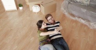 İki mutlu genç insan yeni bir dairede yerde uzanıyor ve cep telefonuyla selfie çekiyor..