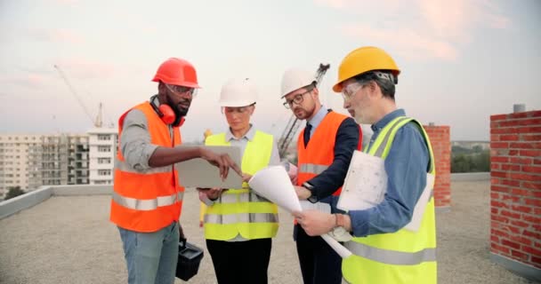 Maschi multietnici e costruttori femminili con progetto di piano di costruzione e computer portatile parlando sul cantiere. Lavoratori edili e investitori, costruttori di razze miste. — Video Stock