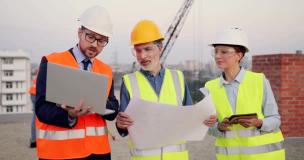 Hombres caucásicos y mujeres constructoras, arquitecta e ingeniera con proyecto de plan de construcción y tableta dispositivo hablando en el sitio de construcción. Arquitecto e inversor, hombres y mujeres constructores trabajando. — Vídeos de Stock