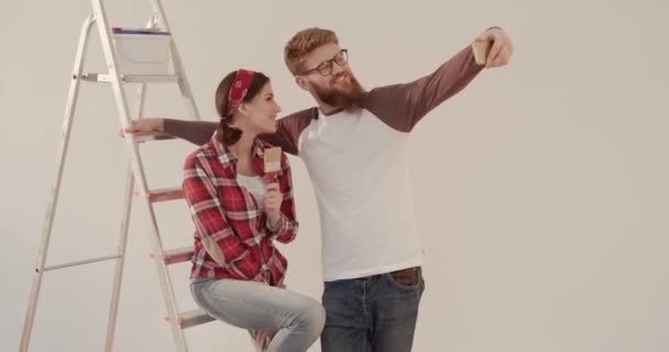 Junges glückliches Ehepaar beim gemeinsamen Familienfoto vor dem Hintergrund von Reparaturen und Leitern. Konzept des Umzugs in neue Wohnung. — Stockvideo