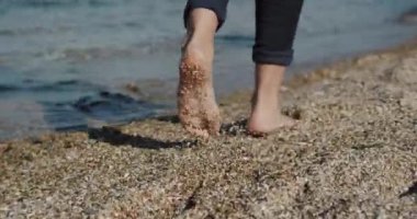 Kameralar, kumlu sahilde yürüyen kadınların ayaklarını takip ediyor. Deniz dalgaları ayaklarını gıdıklıyor. Rıhtım boyunca yürü.