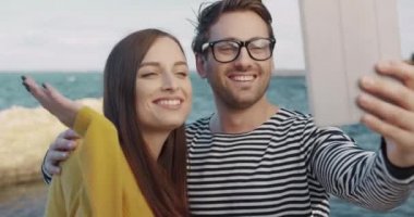 Tablet kullanarak görüntülü iletişim kuran mutlu genç çiftin yakın çekimleri. Neşeli gençler denizde dinleniyor ve izlenimlerini arkadaşlarıyla paylaşıyorlar..