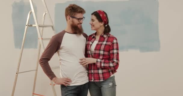 Retrato de casal feliz no novo apartamento abraçando no fundo da parede não pintada olhando para a câmera e sorrindo. — Vídeo de Stock