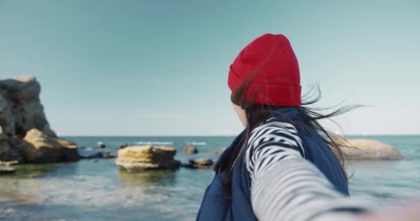 Glad vacker brunett kvinna går till havet håller sina pojkvänner hand och lekfullt tittar på kameran. Följ mig.. — Stockvideo