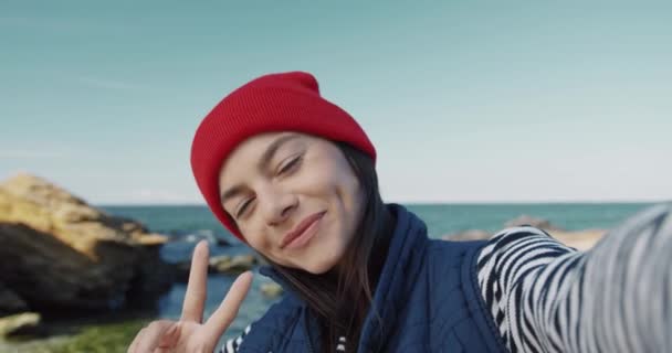 海を背景にカメラを手にポーズをとる若い美少女のクローズアップ。幸せな女の子はビデオで自分自身を撮影することによって悲しみを作ります. — ストック動画
