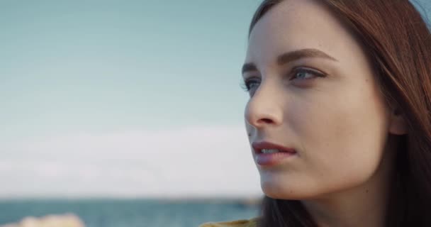 Närbild porträtt av ung vacker kaukasiska kvinna med brunt hår står vid havet och tittar in i fjärran. — Stockvideo