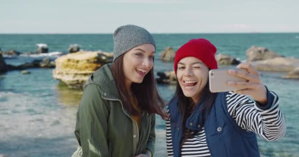 Dvě přítelkyně v kloboucích stojí u moře a berou Selfie. Ženy se baví na dovolené u moře. — Stock video