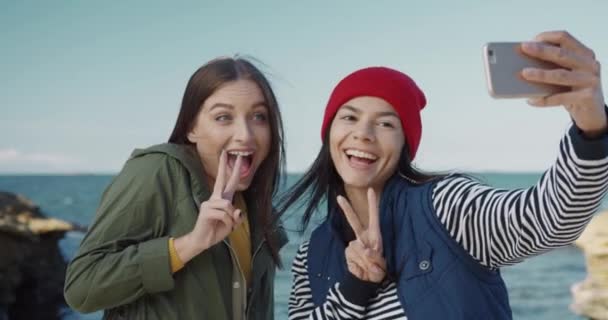 To smukke kaukasiske piger tager selfie på baggrund af havet. Kvindelige venner udgør for smartphone kamera og have det sjovt. – Stock-video