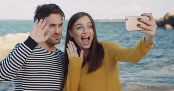 Jovens felizes usam telefone celular para chamadas de vídeo enquanto estão na praia do mar. Casal Cutr compartilha emoções remotamente com amigos. — Vídeo de Stock