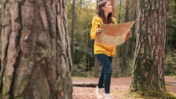 Fiatal lány sárga dzsekiben sétál az erdőben napközben kibontott papírtérképpel. Kutató expedíció. Helyi turizmus. — Stock videók