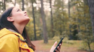 Genç mutlu kadın büyüleyici görünümlü orman, doğada dinleniyor ve akıllı telefon kullanarak sosyal ağlarda haber yayını yapıyor..