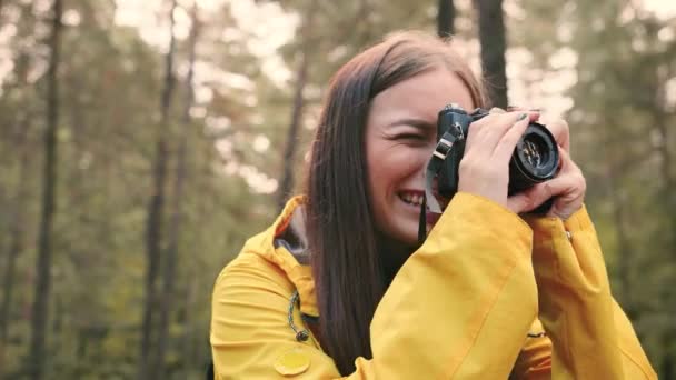 Primo piano di giovane bella ragazza in giacca gialla fa foto della natura sulla sua macchina fotografica in piedi nel bosco. Hobby concetto fotografo. — Video Stock