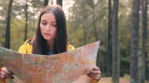 Porträt eines glücklichen Touristenmädchens, das auf einer sonnigen Waldlichtung steht und die Karte in der Hand hält, in die Kamera blickt und lächelt. — Stockvideo