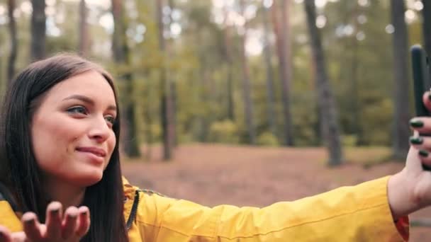 Chica excursionista feliz sentado en el bosque durante el día y hablar con amigos a través de videollamada usando teléfono inteligente. — Vídeo de stock