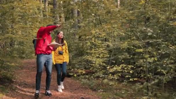 젊은 백인 남자가 여자 친구를 데리고 숲 지역을 걸어서 여행을 하고 있는데, 지도에서 여자 친구의 길을 보여준다. — 비디오