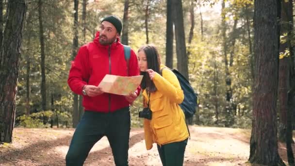 Unga par vandrare står i skogen och försöker förstå området genom att titta på uppfällda papperskarta. — Stockvideo