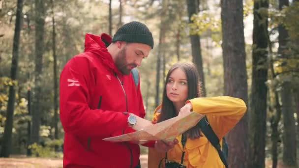 Caméra de gros plan suit deux voyageurs debout dans la forêt et à la recherche d'un moyen à l'aide de la carte papier et pointant à la main. — Video