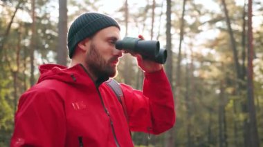 Şapkalı ve kırmızı ceketli yakışıklı beyaz adamın park yerinde dikilip dürbünle bakmasının keyfini çıkarmasını..